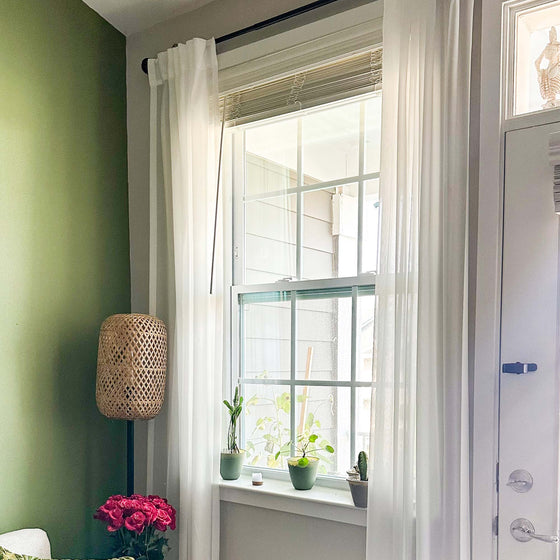 Weiß,Fenster mit weißen Vorhängen, Pflanzen und einem Korb an einer grünen Wand.