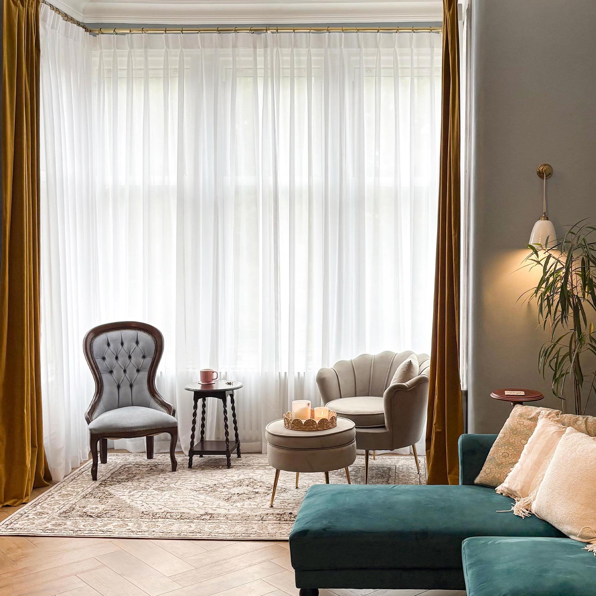 Weiß, Wohnzimmer mit blaugrünem Sofa, grauem Sessel und beigem Sessel neben großen Fenstern mit weißen transparenten und goldenen Vorhängen.